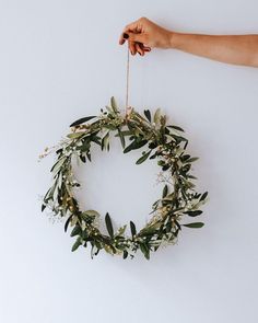 a hand holding a green wreath with white flowers and greenery hanging from the side