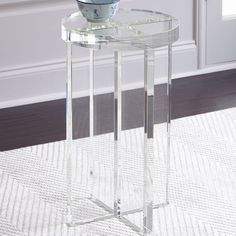 a glass table with a bowl on top and a white rug in front of it