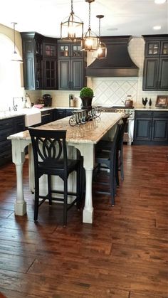 a large kitchen with wooden floors and black cabinets, an island in the center is flanked by two bar stools