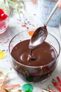 a spoon is pouring chocolate sauce into a glass bowl with confetti on the side