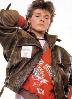 a young man in an orange shirt and leather jacket with his hands on his head