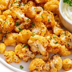 a white plate topped with cauliflower next to a small bowl of ranch dressing