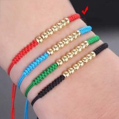 four different colored bracelets on someone's arm with gold beads and black cord