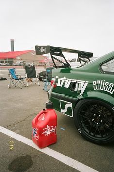 a green car parked in a parking lot next to a red gas can and some chairs