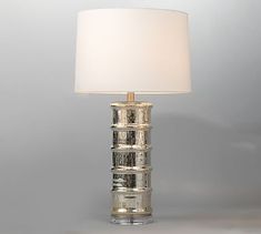 a lamp with a white shade on it sitting on top of a table next to a gray wall