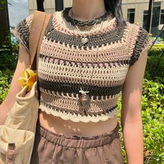 a woman wearing a crocheted top and holding a banana in her right hand