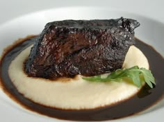 a piece of steak on top of mashed potatoes with sauce and garnish