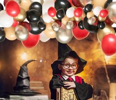 a young boy dressed as harry potter holding a hogwarts sign under balloons and streamers