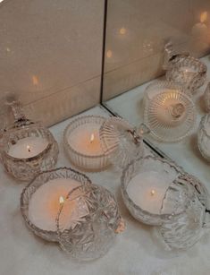 candles are sitting in front of a mirror on the floor next to some glass dishes