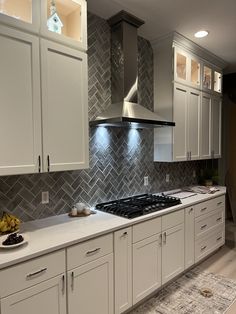 a kitchen with white cabinets and gray tile backsplash, an oven hood over the range