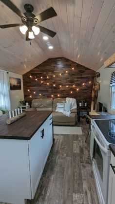 a kitchen and living room with wood paneling on the walls, ceiling fan, stove top oven and sink