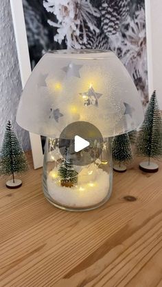 a glass jar filled with snow and christmas lights sitting on top of a wooden table