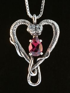 "Cast in solid sterling silver, two snakes entwine to form a Heart. A brilliant 9mm x 6mm gemstone is set in the center of the entwining snakes. Gift yourself or your special someone this unique Valentine as a pledge of your love. Dimensions are 1 1/4\" high and 7/8\" across. Please select your desired gemstone in the dropdown options menu. You may choose between a Blue Topaz, Citrine, Amethyst, Peridot, Mozambique Garnet or Black Onyx, or for an additional price, a Rhodolite Garnet. Although we Snake Chain Jewelry For Valentine's Day Anniversary, Elegant Sterling Silver Snake Jewelry, Unique Snake-shaped Jewelry For Anniversary, Unique Snake Shaped Jewelry For Anniversary, Sterling Silver Snake Jewelry For Anniversary, Snake Heart, Cast Jewelry, Two Snakes, Serpent Necklace