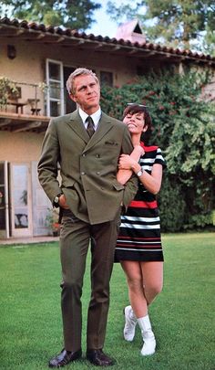 a man in a suit and tie standing next to a woman on the grass near a house