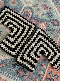 two pieces of black and white crochet sitting on top of a colorful rug