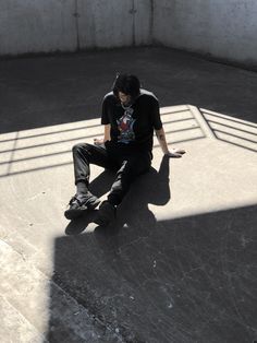 a skateboarder sitting on the ground using his cell phone and looking at his watch