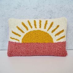 a pillow with the sun painted on it sitting on a white table next to a wall