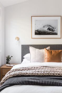 a bed with pillows and blankets on top of it next to a framed mountain photo