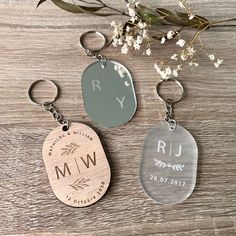 three personalized wooden key chains with initials and date engraved on them, sitting next to some flowers