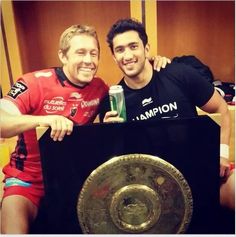 two men are posing for a photo with a trophy and beer in front of them