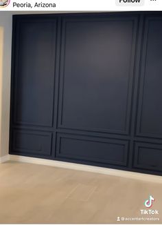 an empty room with dark blue walls and wood flooring in front of a white wall