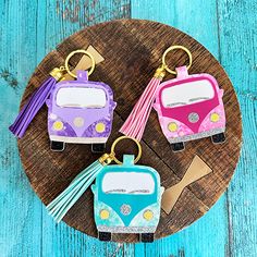 three keychains made to look like campers on a wooden board with tassels hanging from them