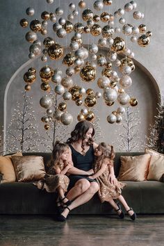 a woman and two children sitting on a couch in front of a christmas tree with ornaments hanging from the ceiling