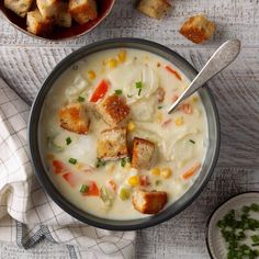 a bowl of soup with croutons and corn on the side next to bread