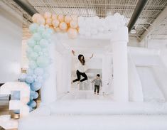 a woman and child are jumping on an inflatable structure with balloons around it