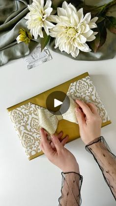 a woman opening a gold envelope with white flowers on it and wrapping the paper around her