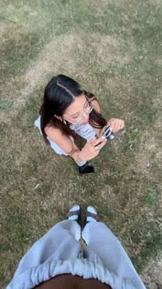 two people sitting in the grass looking at their cell phones and taking pictures with them