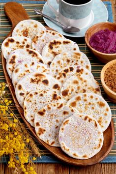 several flat breads on a wooden platter next to bowls of spices and a cup of coffee