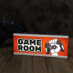 an orange game room sign sitting on top of a wooden table next to a black controller