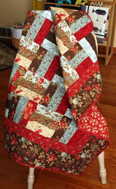 a red and brown quilt sitting on top of a wooden floor next to a chair