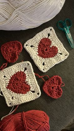 three crocheted squares with yarn and scissors on the floor next to them are red hearts