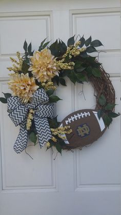 a football wreath is hanging on the door with flowers and greenery around it,