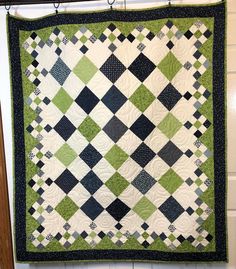 a green and black quilt hanging on a wall