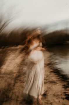 a blurry photo of a woman in white dress standing on the beach near water