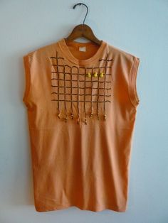 "Sleeveless orange cotton t-shirt hand-embroidered with a black grid pattern. Embellished with three yellow pineapple buttons and black, yellow and orange painted wooden beads. It measures 36\" at the bust and 40\" at the hem. It's 27\" from the neck/shoulder point to the hem.  It was made in 1984 by Okie Dokie Clothes of Toronto." Yellow Sleeveless Cotton T-shirt, Embroidered Orange Cotton Top, Orange Embroidered Cotton Top, Yellow Pineapple, Okie Dokie, Women Magazines, Grid Pattern, Embroidered Tshirt, Wooden Beads