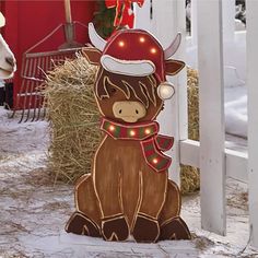 a wooden cow with christmas lights on it's head sitting in front of a white fence