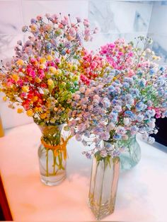 two vases filled with colorful flowers sitting on a table next to each other in front of a mirror