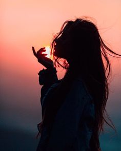 the silhouette of a woman with long hair blowing in the wind, holding her hand out