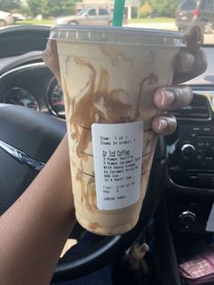 a person holding up a coffee cup in their hand while sitting in a car with the steering wheel behind them