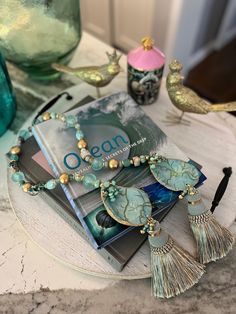 a table topped with books and jewelry on top of a marble countertop next to a bird figurine