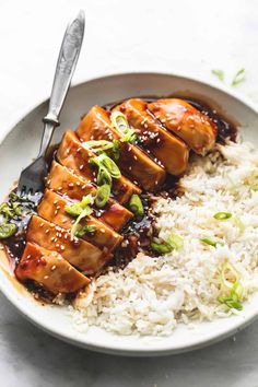 a white plate topped with rice and meat covered in sauce next to a fork on top of it