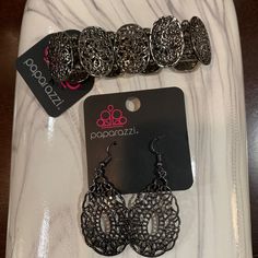 two pairs of earrings are sitting on a white plate next to a black and silver tag