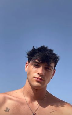 a shirtless man with no shirt on standing in front of a blue sky and looking at the camera