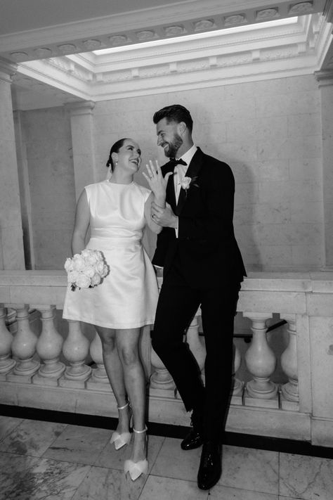 Black and white wedding photo of bride in a shoer wedding dress with bow wedding shoes, round white rose wedding bouquet flashing her wedding ring with the groom in a black tuxedo at classic and timeless registry office wedding | city wedding | wedding photography | Joan Jellet Photography Wedding Registry Photography, Registry Wedding Photography, Registry Office Wedding Photos, London Registry Office Wedding, Registry Office Wedding Dress, Bow Wedding Shoes, Wedding Dress With Bow, White Rose Wedding, Photo Of Bride