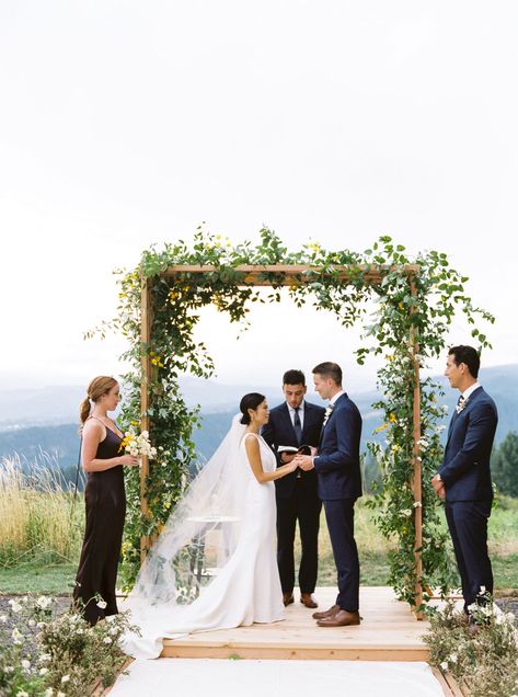 Wooden structure with greenery and wildflowers for wedding ceremony arch at Georgecrest Vineyards in Washington planned by Beth Helmstetter. Beth Helmstetter events destination wedding with wooden platform, outdoor wedding with mountain view. Vineyard Wedding Ceremony Arch, Wooden Wedding Arch With Greenery, Wedding Alter Stage, Wedding Ceremony Platform Stage, Wedding Platform Decorations, Outdoor Wedding Stage Ideas, Simple Greenery Wedding Arch, Wedding Platform Stage, Wedding Ceremony Platform