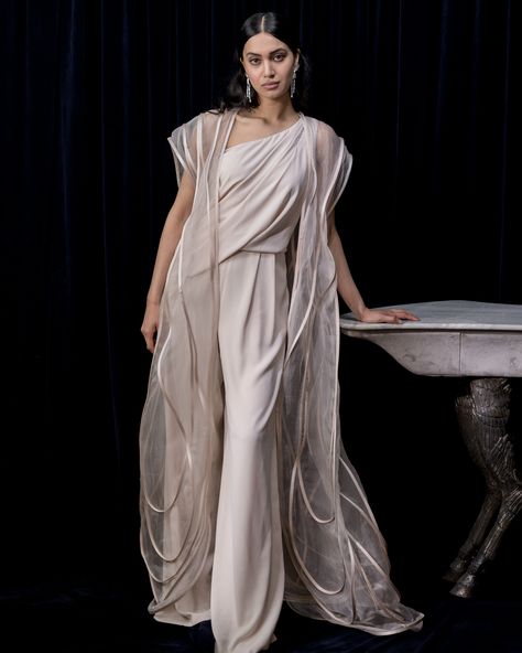 Comfort Couture; A draped one-shoulder flared  jumpsuit is complemented with a sheer sculpted organza long cape. In keeping with the monochromatic look, skip the accessories and add strappy heels, tall earrings with pushed back hair  #GauravGupta #GauravGuptaCouture #Co-ords #DestinationWedding #signature #luxury #MadeInIndia #OccasionWear Pushed Back Hair, Draped Saree Gown, Ethereal Romantic, Flared Jumpsuit, Monkey Mind, Gaurav Gupta, Organza Gowns, Long Cape, Collection Ideas